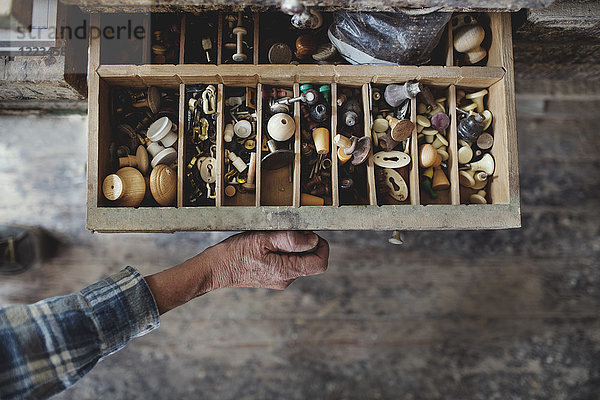 Abgeschnittenes Bild des Handwerkers beim Öffnen der Schublade mit Knöpfen in der Werkstatt