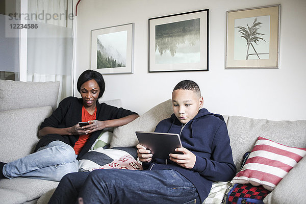 Mutter und Sohn mit Technologien auf dem Sofa zu Hause