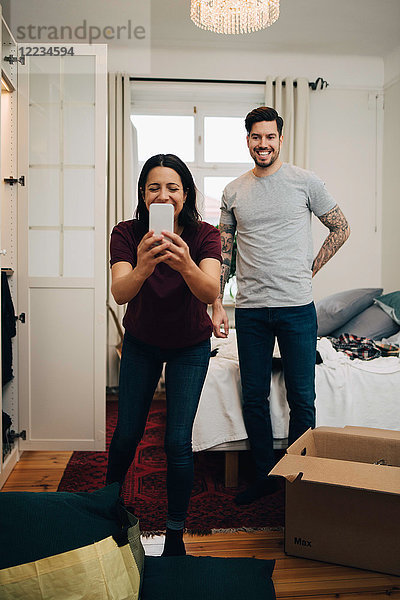 Frau nimmt Selfie auf dem Handy  während sie mit dem Mann im Schlafzimmer steht.