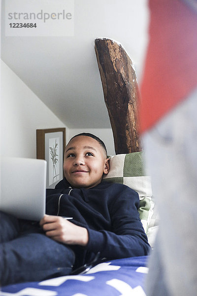 Teenager Junge mit Laptop auf dem Bett liegend  während er die Mutter im Haus ansieht.