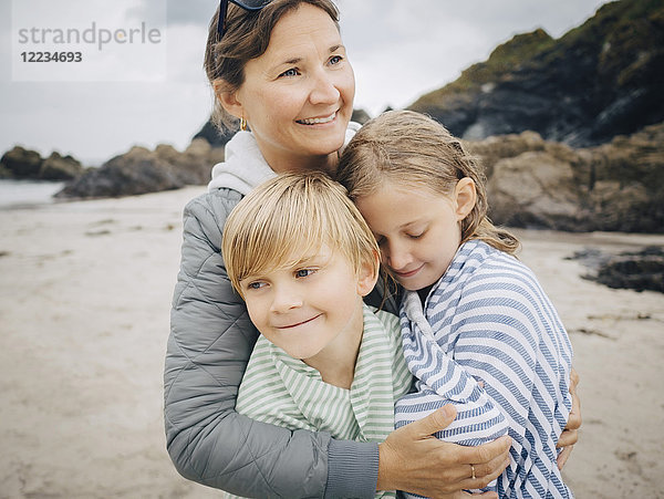 Lächelnde Frau umarmt Kinder  die am Strand stehen.