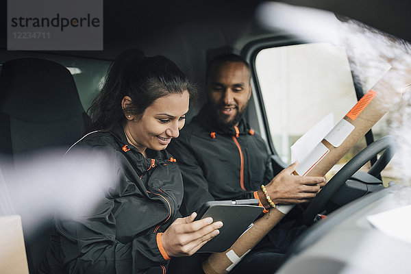 Lächelnde Arbeiter  die im Lieferwagen auf das digitale Tablett schauen