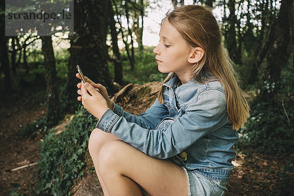 Seitenansicht des blonden Mädchens mit Smartphone im Wald