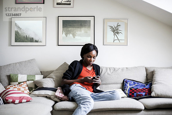 Mittlere erwachsene Frau mit Smartphone auf dem Sofa zu Hause