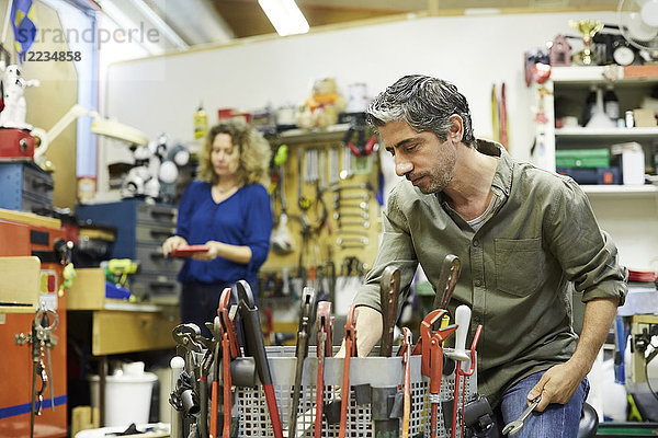 Reife männliche Freiwillige  die mit Werkzeugen gegen weibliche Kollegen in der Werkstatt arbeiten.