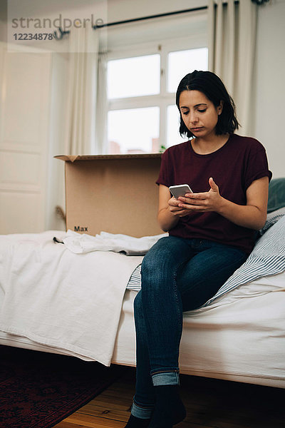 Frau  die ein Handy benutzt  während sie auf dem Bett sitzt.