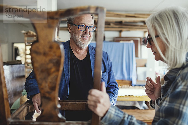 Senior-Besitzer zeigt Holzstuhl dem männlichen Kunden in der Werkstatt