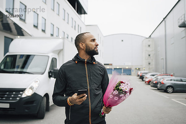 Männlicher Arbeiter mit Blumenstrauß und Smartphone bei der Suche in der Stadt