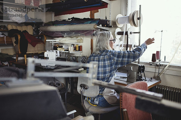 Seniorchef mit Nähmaschine am Tisch in der Werkstatt