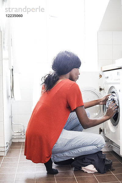 Durchgehende Seitenansicht der mittleren erwachsenen Frau beim Wäschewaschen zu Hause