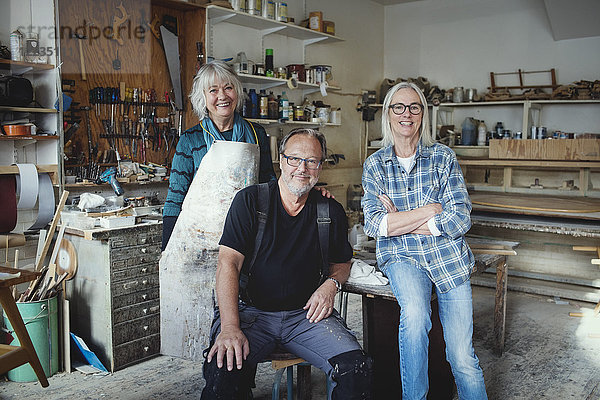 Porträt von lächelnden Seniorinnen und Seniorinnen  die in der Werkstatt gegen Werkzeuge stehen