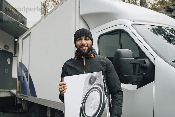 Porträt eines lächelnden Mannes  der die Kiste hält  während er gegen den Lieferwagen steht.