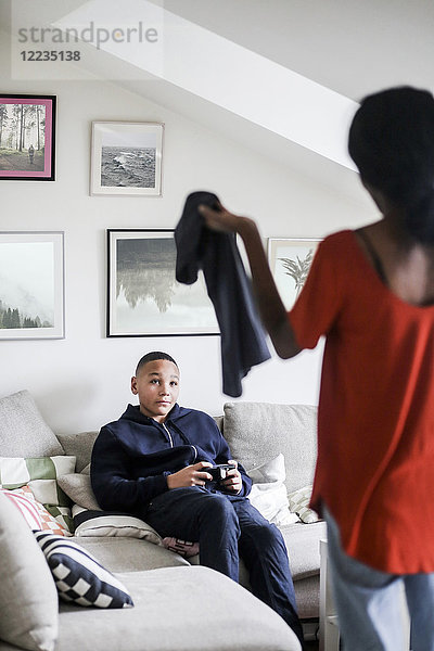 Teenager-Junge schaut Mutter mit T-Shirt im Wohnzimmer an.