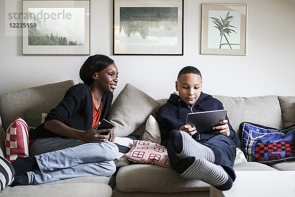 Volle Länge der Mutter  die den Sohn mit einem digitalen Tablett auf dem Sofa zu Hause betrachtet.