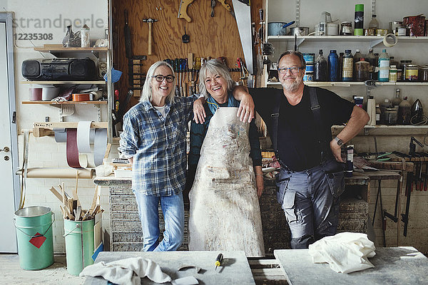 Porträt von fröhlichen Senior-Mitarbeitern  die in der Werkstatt gegen Werkzeuge stehen