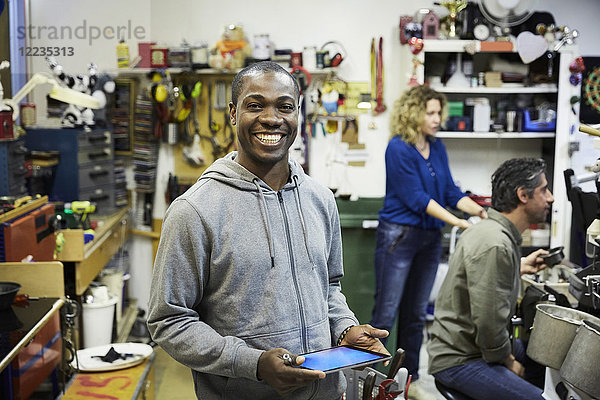 Porträt eines lächelnden Freiwilligen mit digitalem Tablett und Kollegen  die in der Werkstatt arbeiten.