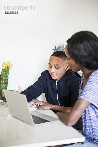Mutter hilft Sohn bei den Hausaufgaben mit Laptop auf dem Tisch zu Hause