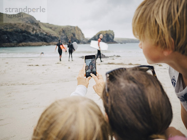 Frau nimmt Selfie mit Kindern vom Handy am Strand mit.