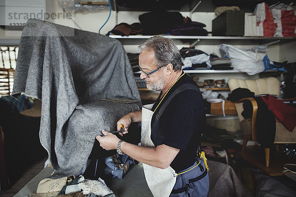Senior männlicher Besitzer schneidet grauen Stoff  während er in der Werkstatt steht.