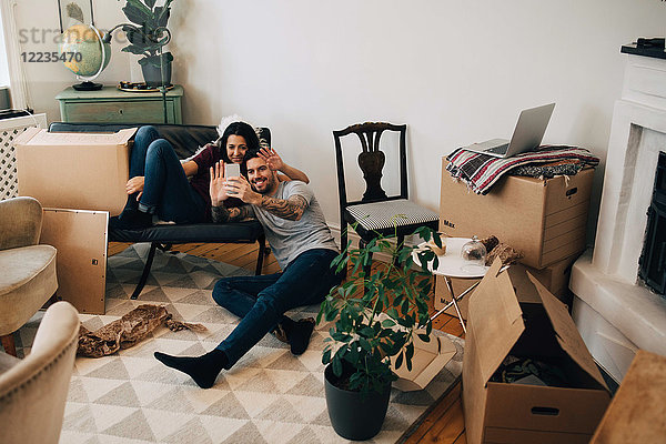 Lächelndes Paar Videoanrufe über Handy während des Umzugs im Wohnzimmer