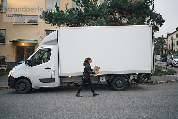 Arbeiterin  die eine Kiste trägt  während sie mit dem Lieferwagen auf der Straße in der Stadt unterwegs ist.