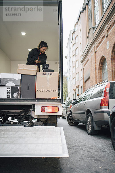 Arbeiterin mit digitalem Tablett bei der Analyse von Paketen im Lieferwagen in der Stadt