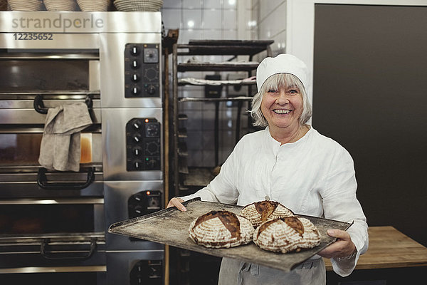 Lächelnder Bäcker mit frisch gebackenem Brot in der Backstube