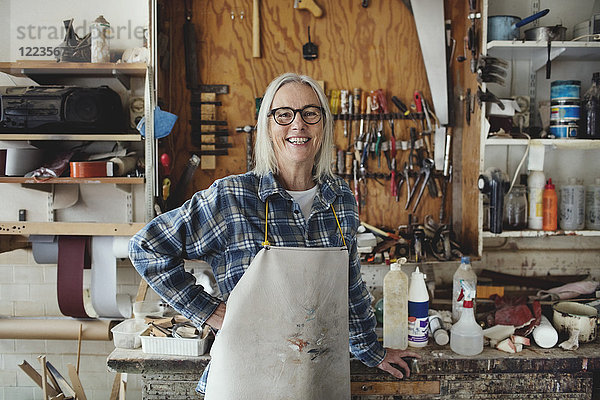 Porträt eines lächelnden Seniorbesitzers  der sich in der Werkstatt gegen Werkzeuge stellt