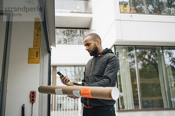 Männlicher Bote mit einem Paket  das ein Mobiltelefon benutzt  während er im Lieferwagen steht