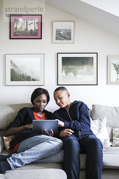 Mutter und Sohn mit digitalem Tablett auf dem Sofa zu Hause