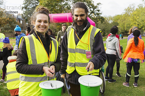 Portrait lächelnde Freiwillige mit Spendeneimern beim Benefizlauf im Park