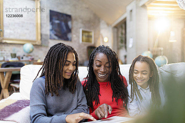 Lächelnde Mutter und Töchter beim Betrachten des Fotoalbums auf dem Sofa