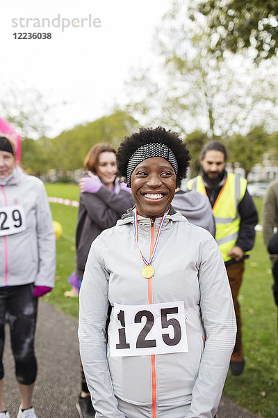 Portrait lächelnde  selbstbewusste Läuferin mit Medaille beim Charity-Lauf im Park