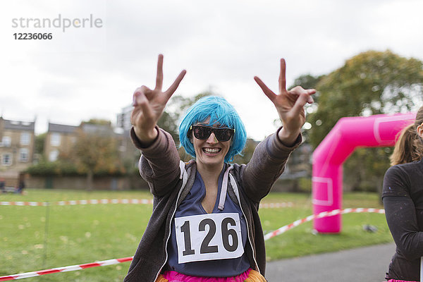 Portrait begeisterte Läuferin in Perücke gestikulierend Friedenszeichen beim Charity-Lauf im Park
