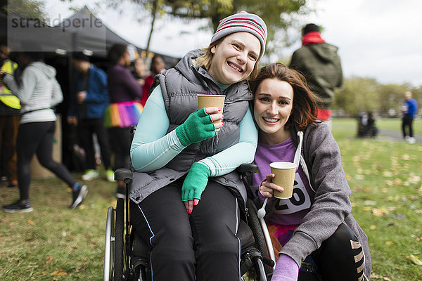 Portrait lächelnde Frau im Rollstuhl mit Freundin  Trinkwasser beim Benefizrennen im Park