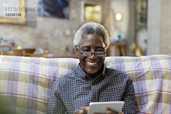 Lächelnder älterer Mann mit digitalem Tablett auf dem Sofa