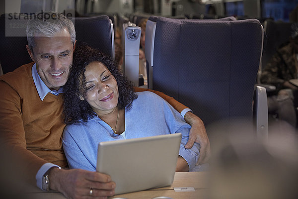 Liebevolles Paar  das sich nachts einen Film auf einem digitalen Tablett im Personenzug ansieht.