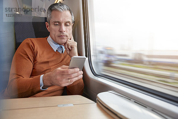 Fokussierter Geschäftsmann mit Smartphone am Personenzugfenster
