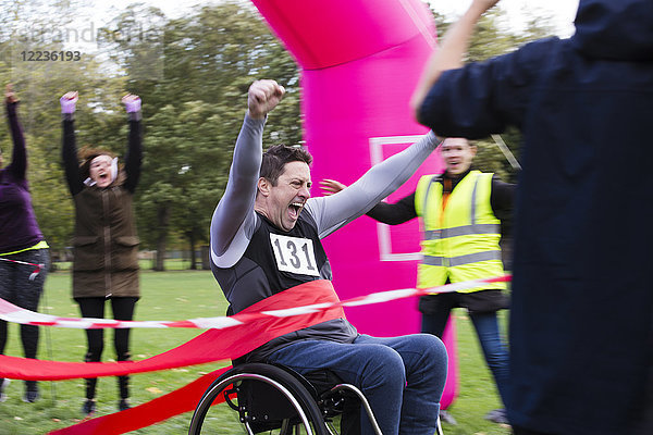 Enthusiastischer Mann im Rollstuhl überquert die Ziellinie des Charity-Rennens