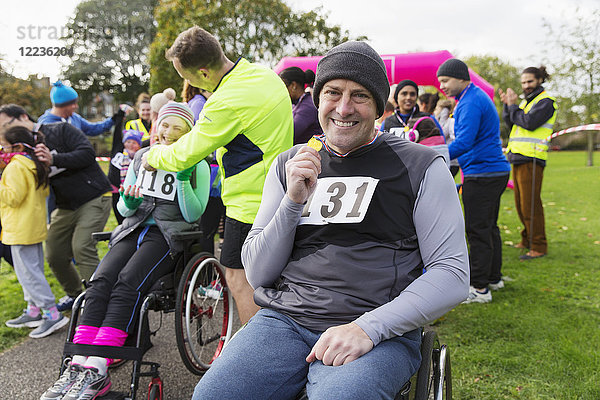 Portrait lächelnder  selbstbewusster Mann im Rollstuhl mit Medaille beim Charity-Rennen im Park