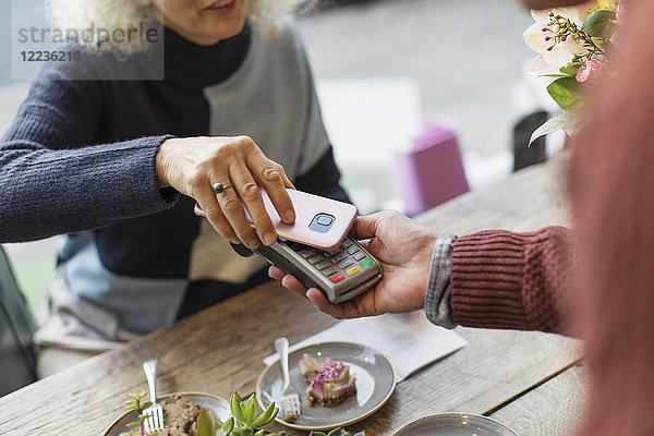 Frau mit Smartphone mit kontaktloser Bezahlung im Cafe