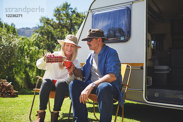 Aktives Seniorenpaar trinkt Kaffee außerhalb des Wohnmobils auf dem sonnigen Sommercampingplatz.