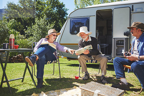 Aktive Seniorenfreunde beim Lesen vor dem Wohnmobil auf dem sonnigen Sommercampingplatz