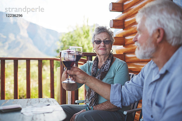 Aktives Seniorenpaar beim Rösten von Rotweingläsern auf dem Balkon