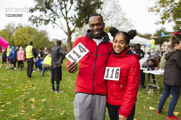 Porträt lächelnde  selbstbewusste Vater- und Tochterläufer mit Marathon-Lätzchen beim Charity-Lauf im Park