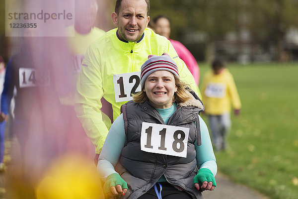 Portrait Mann schiebt lächelnde Frau im Rollstuhl beim Charity-Rennen im Park