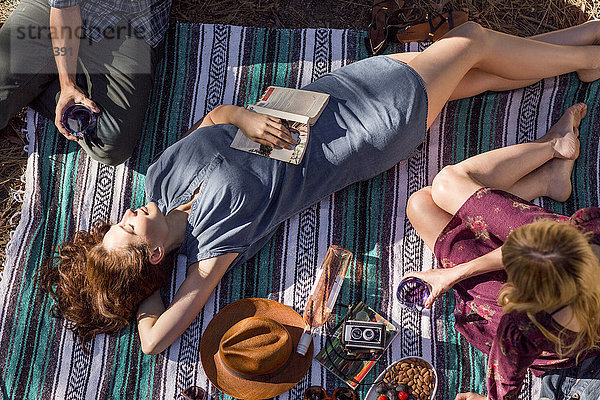 Draufsicht junge Frau mit Buch zum Entspannen auf Picknickdecke