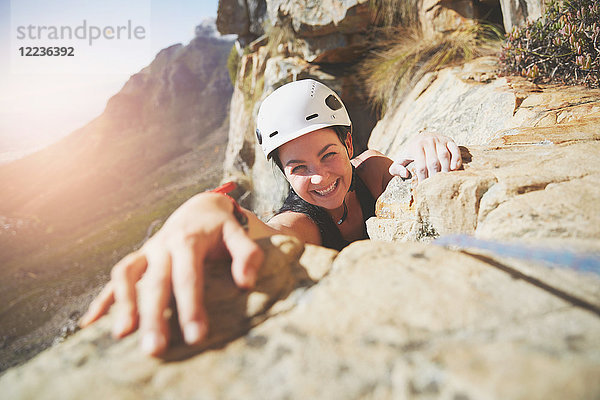 Porträt lächelnder  selbstbewusster Kletterer  der nach dem Fels greift.