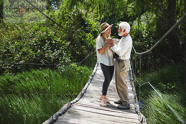 Romantisch aktives Seniorenpaar hält sich an der idyllischen Fußgängerbrücke fest.