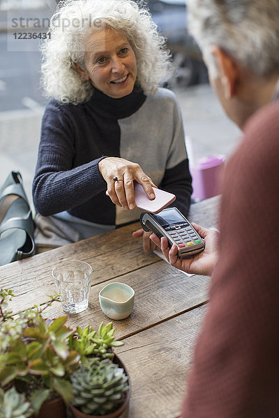 Frau mit Smartphone kontaktlos bezahlen im Cafe